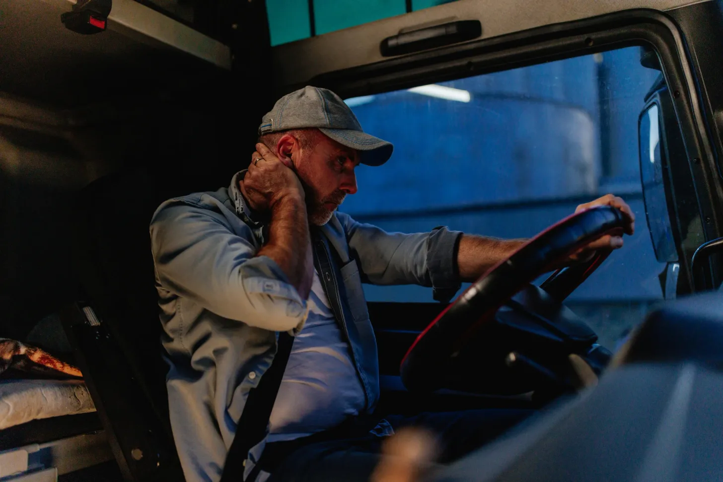 Conductor de camión cansado tomándose la nuca al volante, dentro de la cabina